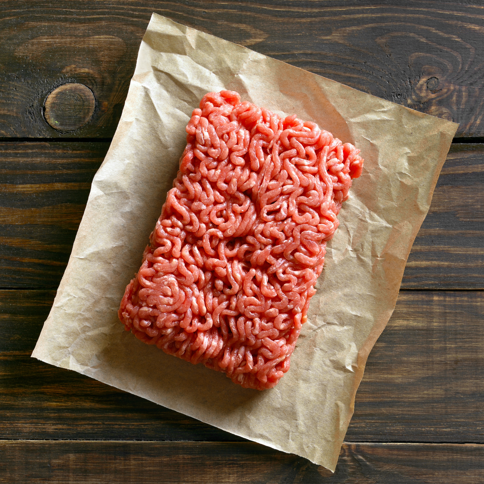 Block of ground beef on parchment paper over a wooden board.