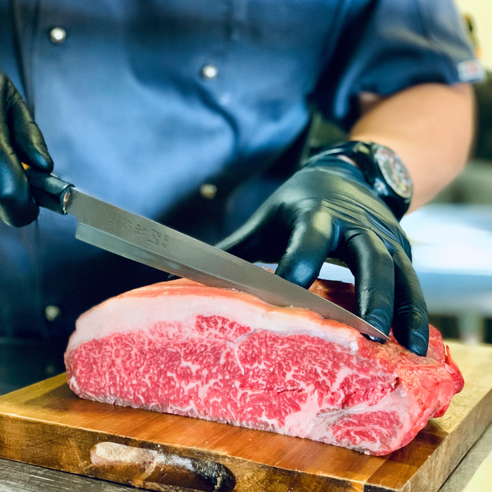 An artisan butcher slicing a heavily marbled raw 100% Fullblood American Wagyu New York strip loin on a wooden cutting board at Winston Cattle Co.'s in-house custom processing plant.