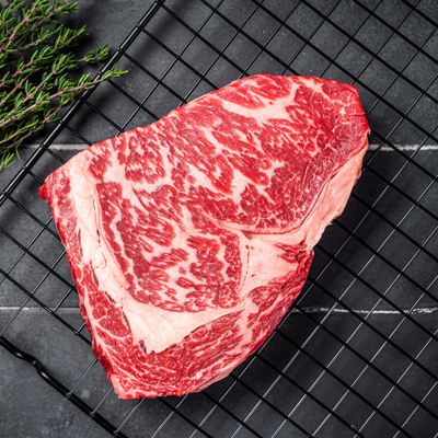 A raw, thickly cut 100% Fullblood American Wagyu ribeye steak resting on a black wire cooling tray, showcasing elite Japanese bloodline intramuscular snowflake marbling at Winston Cattle Co.