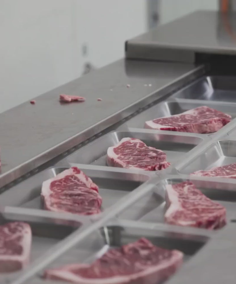 Inside the Winston Cattle Co Fort Worth facility: an automated cutting machine slicing a whole USDA Prime loin into thick, uniform steaks.