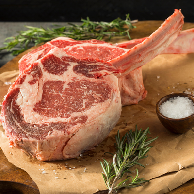 Two raw, thick-cut USDA Prime Black Angus bone-in ribeye steaks seasoned with sea salt and fresh rosemary on butcher paper, processed direct by Winston Cattle Co.