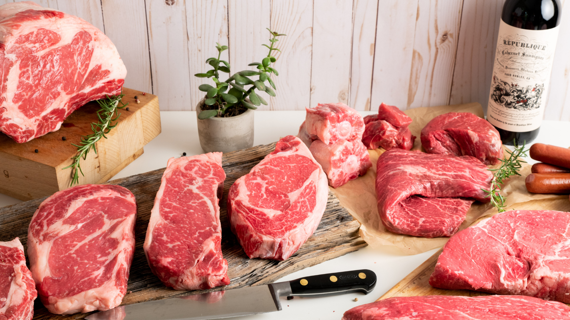 A wide 16:9 cinematic selection of raw, custom-cut USDA Prime Black Angus steaks, roasts, and specialty butcher cuts on a rustic board, representing Winston Cattle Co.'s in-house processing.