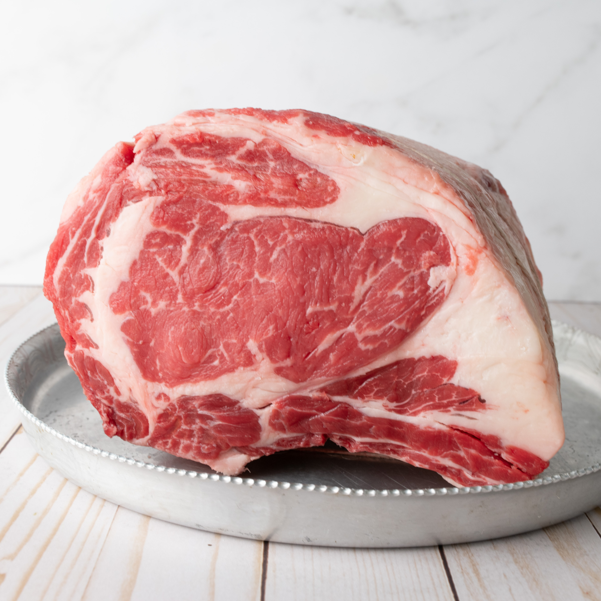 A raw, premium USDA Prime Black Angus prime rib roast showing rich intramuscular marbling and a clean fat cap, custom processed at Winston Cattle Co.